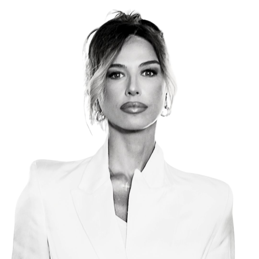 Das Bild zeigt eine Frau in einem weißen Blazer, elegant und selbstbewusst in schwarzes-weißem Stil fotografiert. Sie blickt direkt nach vorne, die Haare locker zurückgebunden