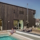 Modern dark wooden house with a swimming pool and sun loungers, person relaxing by the water.