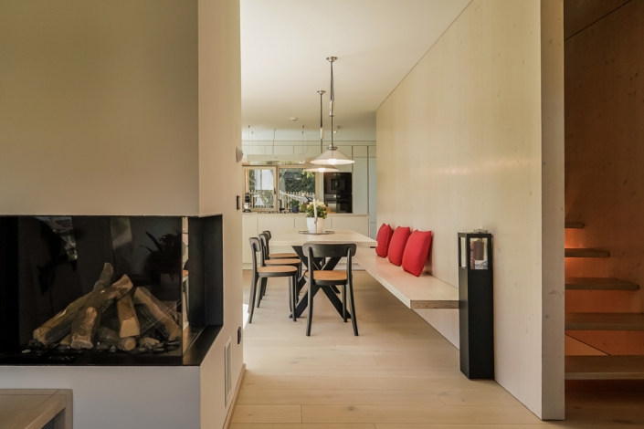 Bright dining area with a wooden table, bench seating with red cushions, and hanging lights.
