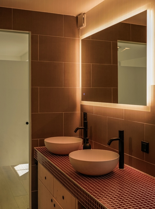 Modern bathroom with two round sinks, dark faucets, and a large illuminated mirror.
