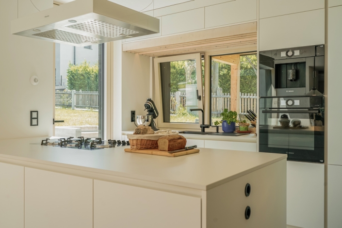Bright kitchen with a cooking island, bread on a cutting board, and a window view to the garden.