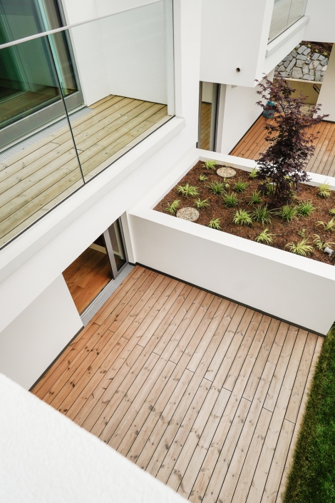 Holzterrasse mit Glasgeländer und bepflanztem Innenhof