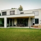 Modern two-story house with large windows, flat roof, and a garden lawn.