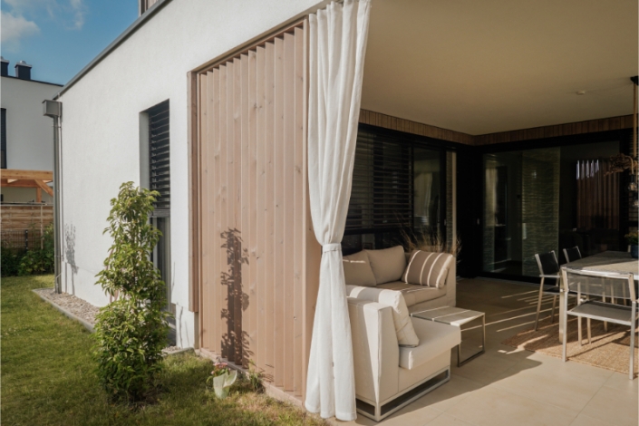 Terrace with white curtains and outdoor seating area by wooden facade.