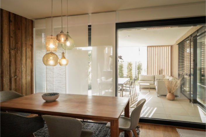 Dining room with wooden table, chairs, and modern hanging lights.